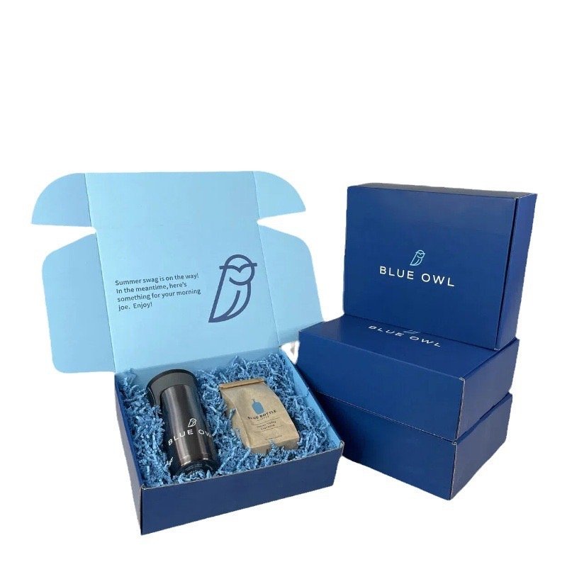 Blue Owl-branded gift box with coffee items and blue shredded filler.