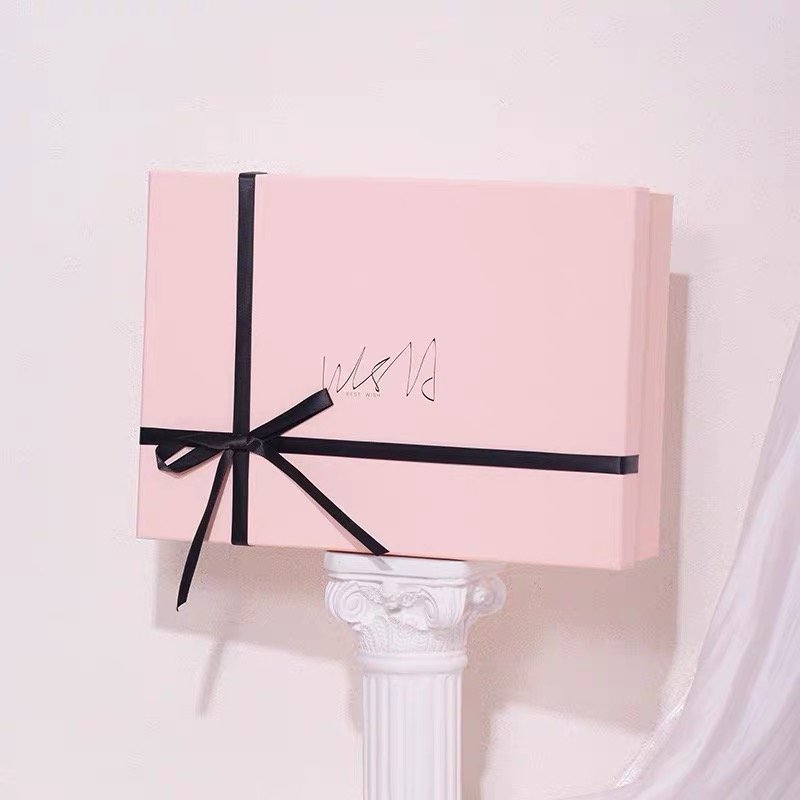 A pastel pink gift box tied with a sleek black ribbon on a decorative pedestal.