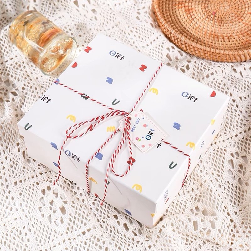 A white gift box with colorful patterns tied with a red and white twine ribbon.