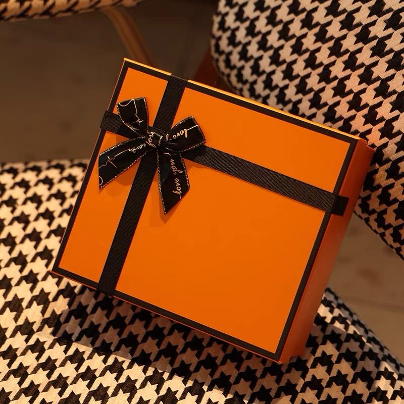 An orange gift box with a black ribbon and bow, placed on a houndstooth-patterned chair.