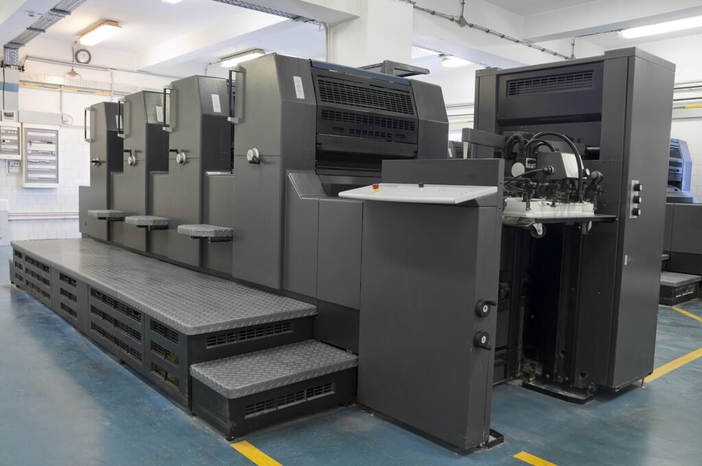A four-color printing press machine in action, showcasing the printing process with cyan, magenta, yellow, and black ink.