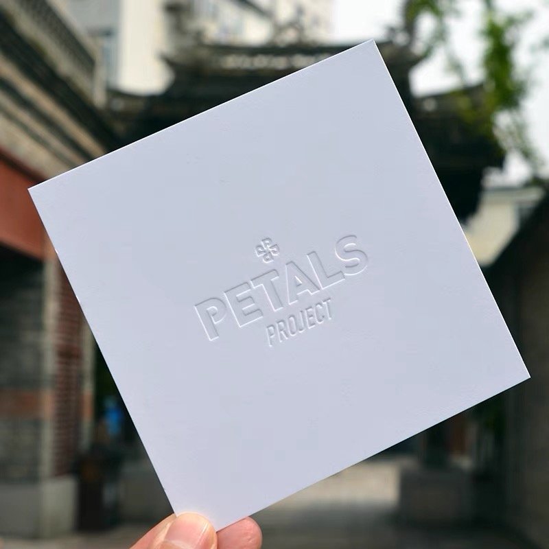 White embossed card with "PETALS PROJECT" logo held in an outdoor setting.