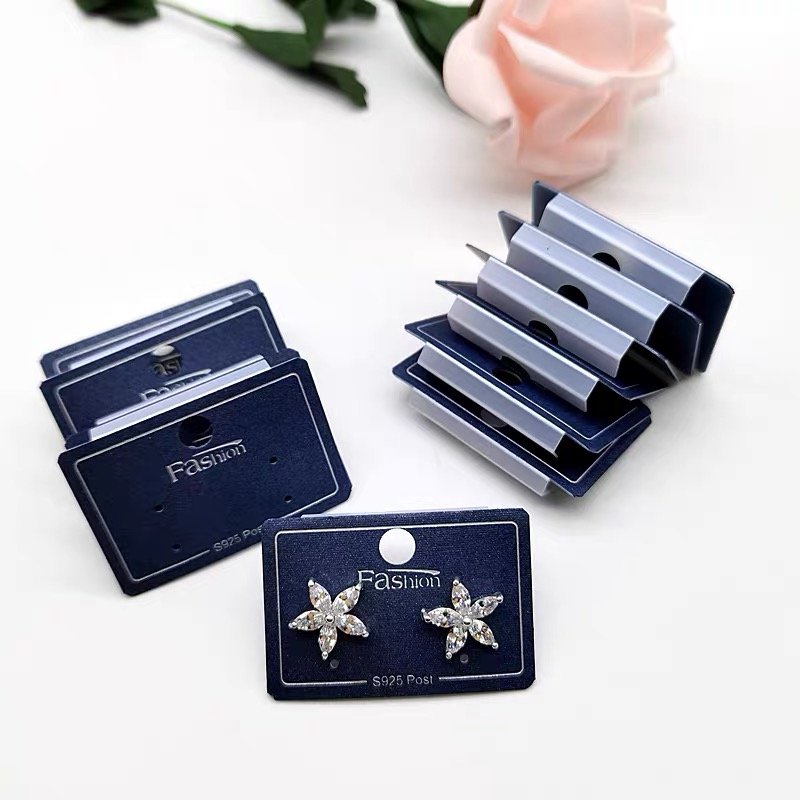 A display of navy-blue earring cards with crystal earrings and stacked packaging on a white surface.